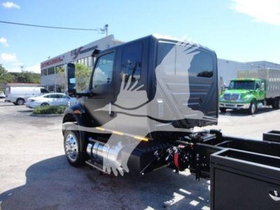 Truck cab and chassis in a dealership lot showing front and side view with hookups and side mirrors.