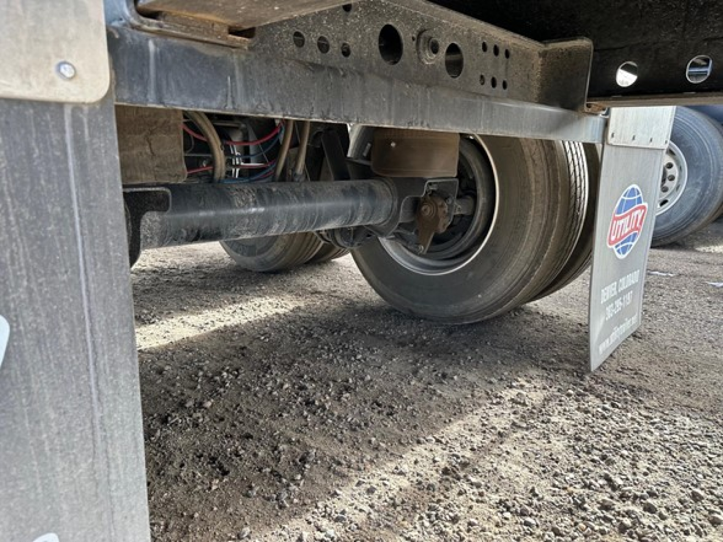 Trailer undercarriage with wheel, suspension, and frame; visible are axles, leaf springs, and a mudflap with US flag logo.