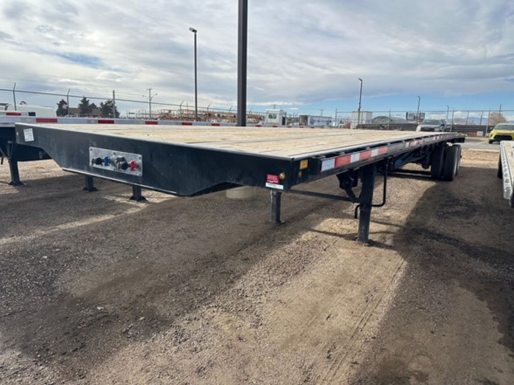 Flatbed trailer with air ride suspension showing front controls and undercarriage; steel deck, black paint, side marker lights, and landing legs visible.