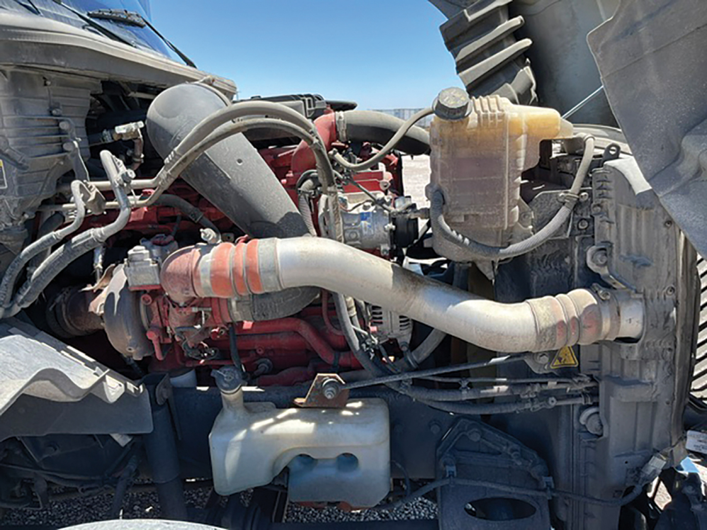 Truck engine bay showing International LT625 diesel engine with red engine block, multiple hoses, and coolant reservoir.
