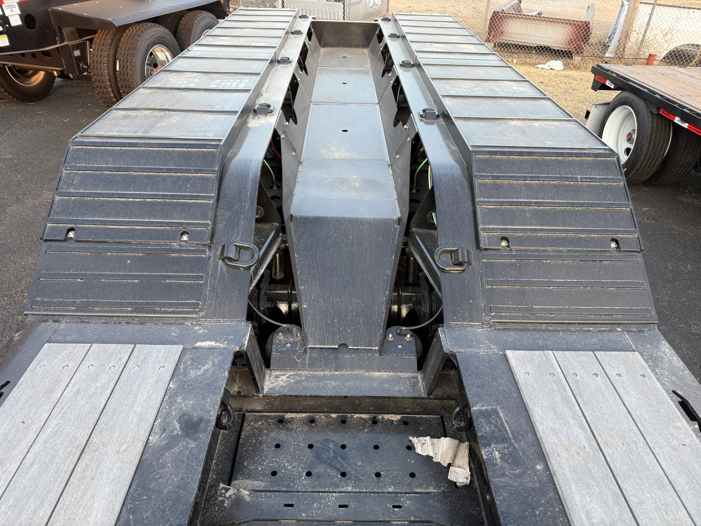 Trailer chassis/view of Load King 554-Quad with dual goosenecks and wide deck, front center hub, metal steps and fenders, visible perforated deck holes, overall rugged steel structure.