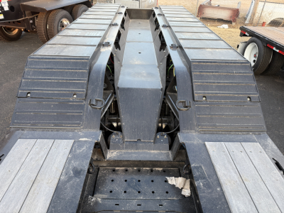 Trailer chassis/view of Load King 554-Quad with dual goosenecks and wide deck, front center hub, metal steps and fenders, visible perforated deck holes, overall rugged steel structure.