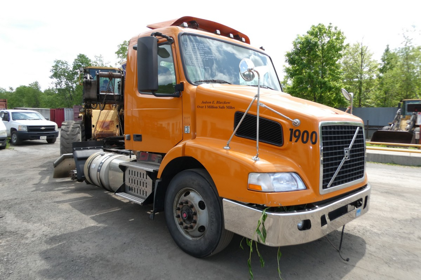 Volvo VNM42T daycab truck in orange with number 1900 on door and front bumper angle view showing fuel tanks and exhaust stack