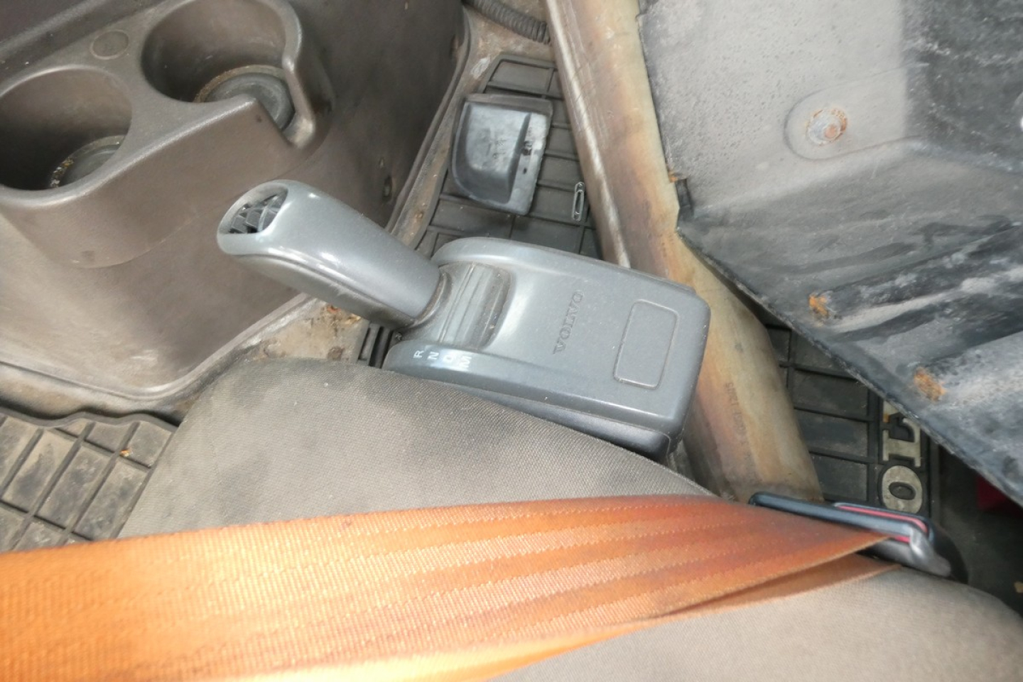 Volvo interior showing parking brake lever and seat belt in cab, cup holders visible.