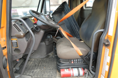  Volvo VNM42T truck cab interior showing steering wheel, dashboard, driver seat, orange seatbelt, and step area with fire extinguisher.