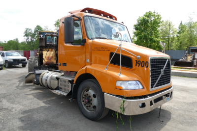 Volvo VNM42T daycab truck in orange with number 1900 on door and front bumper angle view showing fuel tanks and exhaust stack