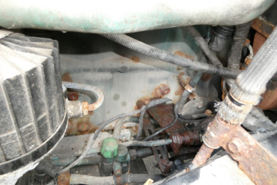 Engine bay view showing hoses, wiring, and rusted components around a Volvo truck engine bay.