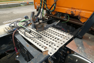 Truck cab area with metal perforated platform and wiring harnesses near engine bay, showing orange vehicle body and adjacent components.