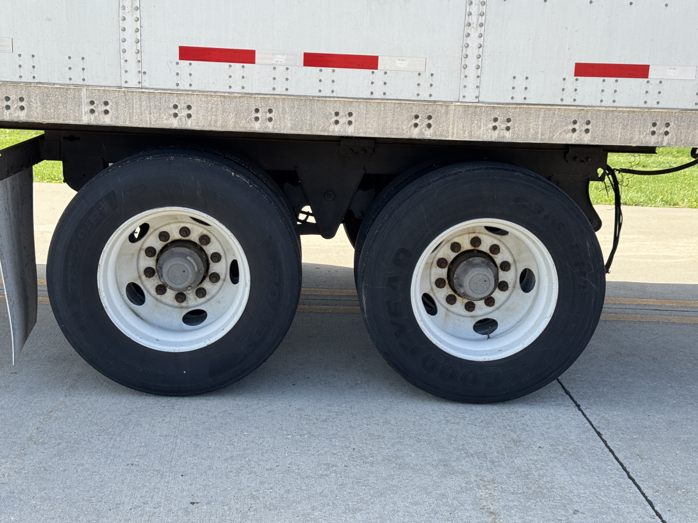 Dual rear axles of a Wabash Duraplate trailer showing white steel wheels and dual tires under a metal sidewall with red reflective markings.