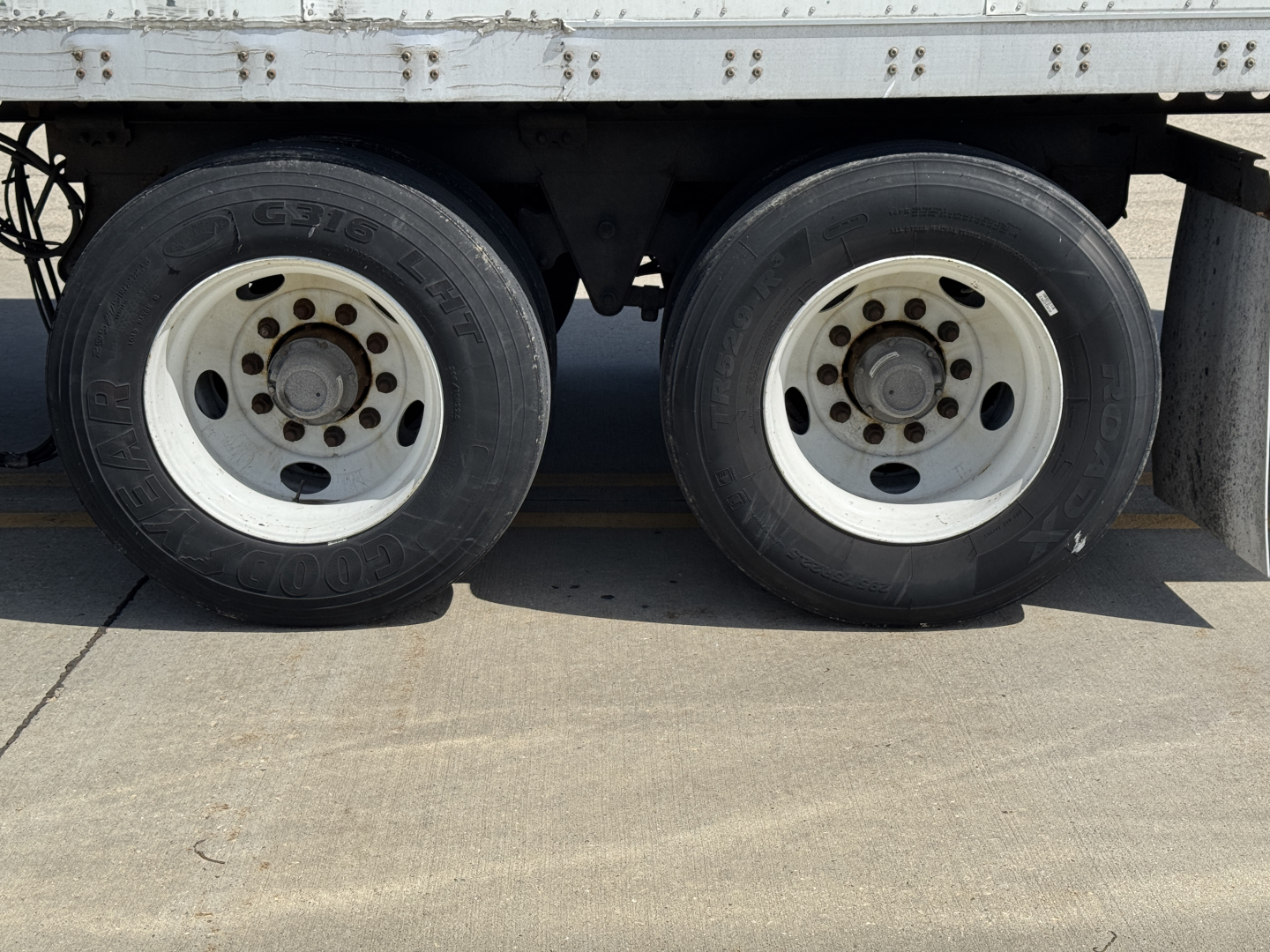 Trailer dual wheels and tires on a Wabash Duraplate trailer showing white rims and solid side rail, undercarriage visible.