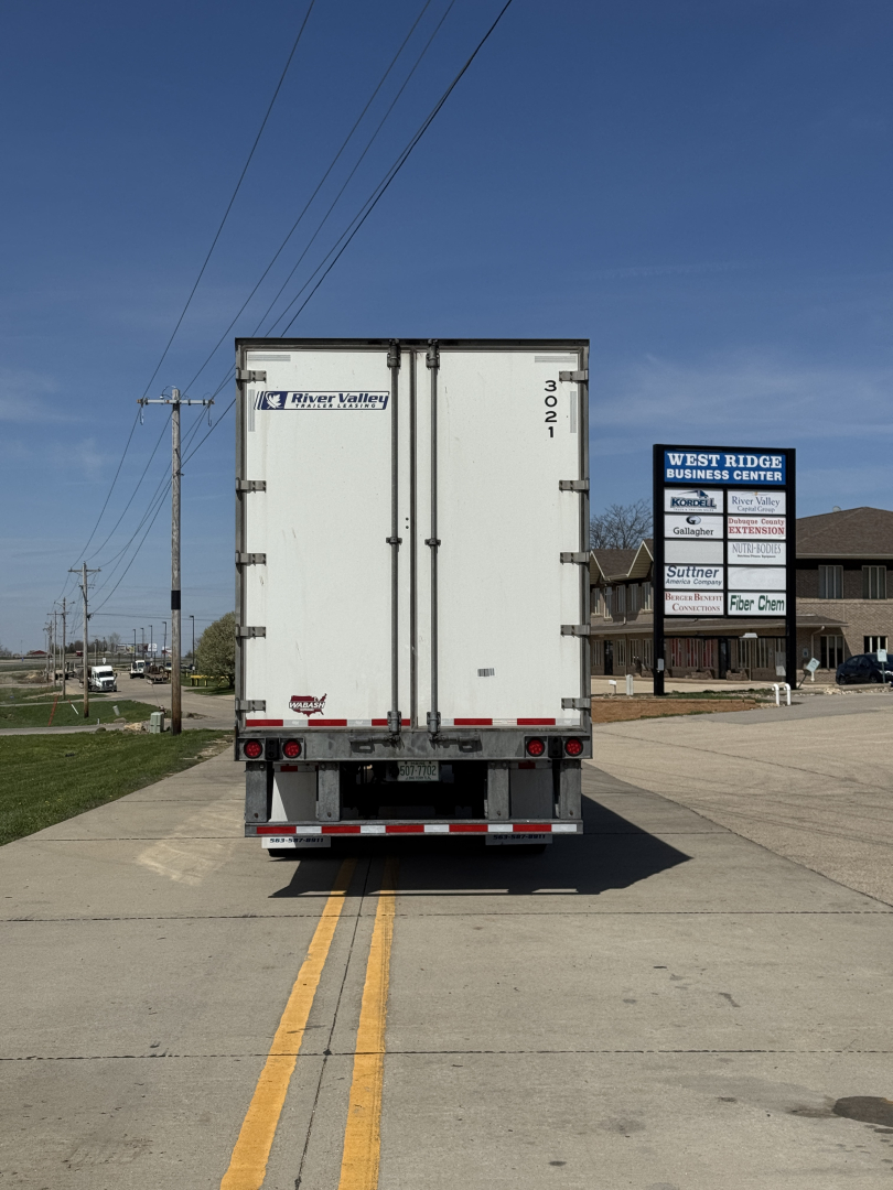 Rear view of a white Wabash Duraplate trailer with doors closed, bumper reflectors, and wheel wells visible, license-plate area not shown, in a truck yard.