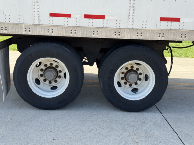 Dual rear axles of a Wabash Duraplate trailer showing white steel wheels and dual tires under a metal sidewall with red reflective markings.