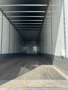 Trailer interior showing empty dry cargo space with metal walls and roof, entry ramp visible at front, weathered floor and ribbed sides.