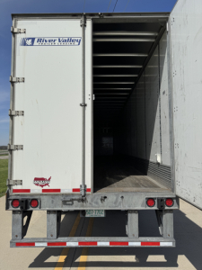 Rear view of a Wabash/Duraplate trailer with open doors showing cargo area and River Valley Transportation & Leasing sticker, trailer lights, and license plate area.