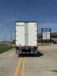Rear view of a white Wabash Duraplate trailer with doors closed, bumper reflectors, and wheel wells visible, license-plate area not shown, in a truck yard.