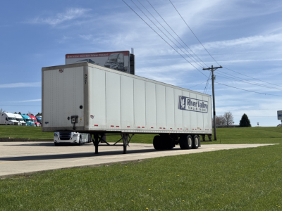 Wabash Duraplate trailer with River Valley Trailers logo on side, elevated front landing gear, license plate area, and a service sign in distance. Clear blue sky.