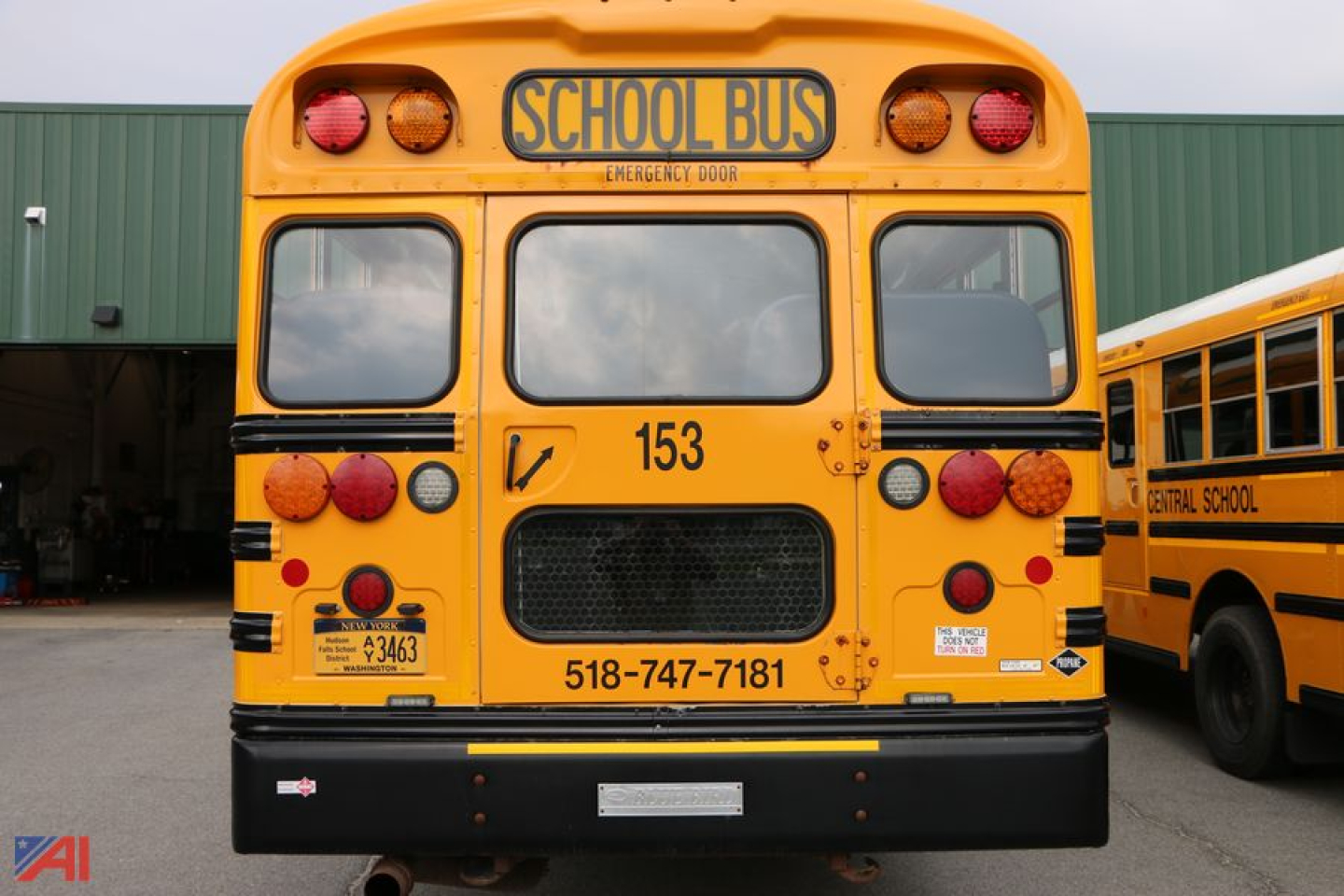 School bus rear view with 'SCHOOL BUS' sign, number 153, and contact phone on the bumper.