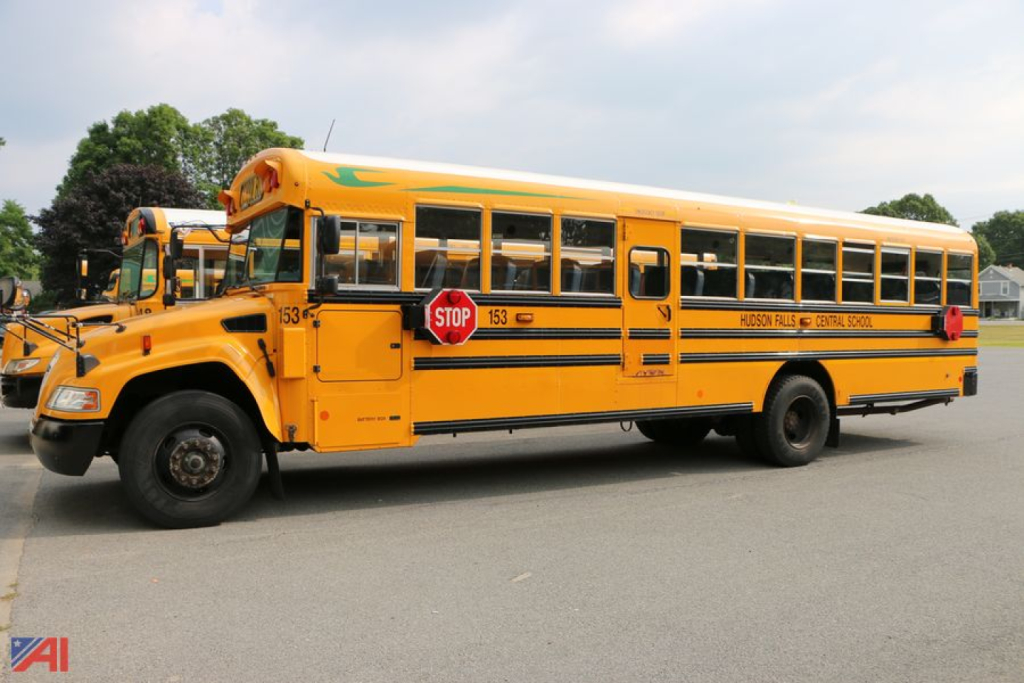 School bus side view showing Stop sign, yellow body, black stripe, model number 153 on door, and text HUDSONVILLE-LITCHFIELD SCHOOLS along the side.