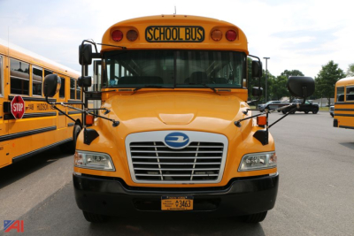 School bus front view showing blue bird logo, yellow body, grille, headlights, and STOP sign/School Bus sign on top; plate visible.