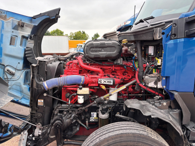 Kenworth T680 Next Gen engine bay showing red Cummins X15 engine with blue coolant hose and surrounding components.