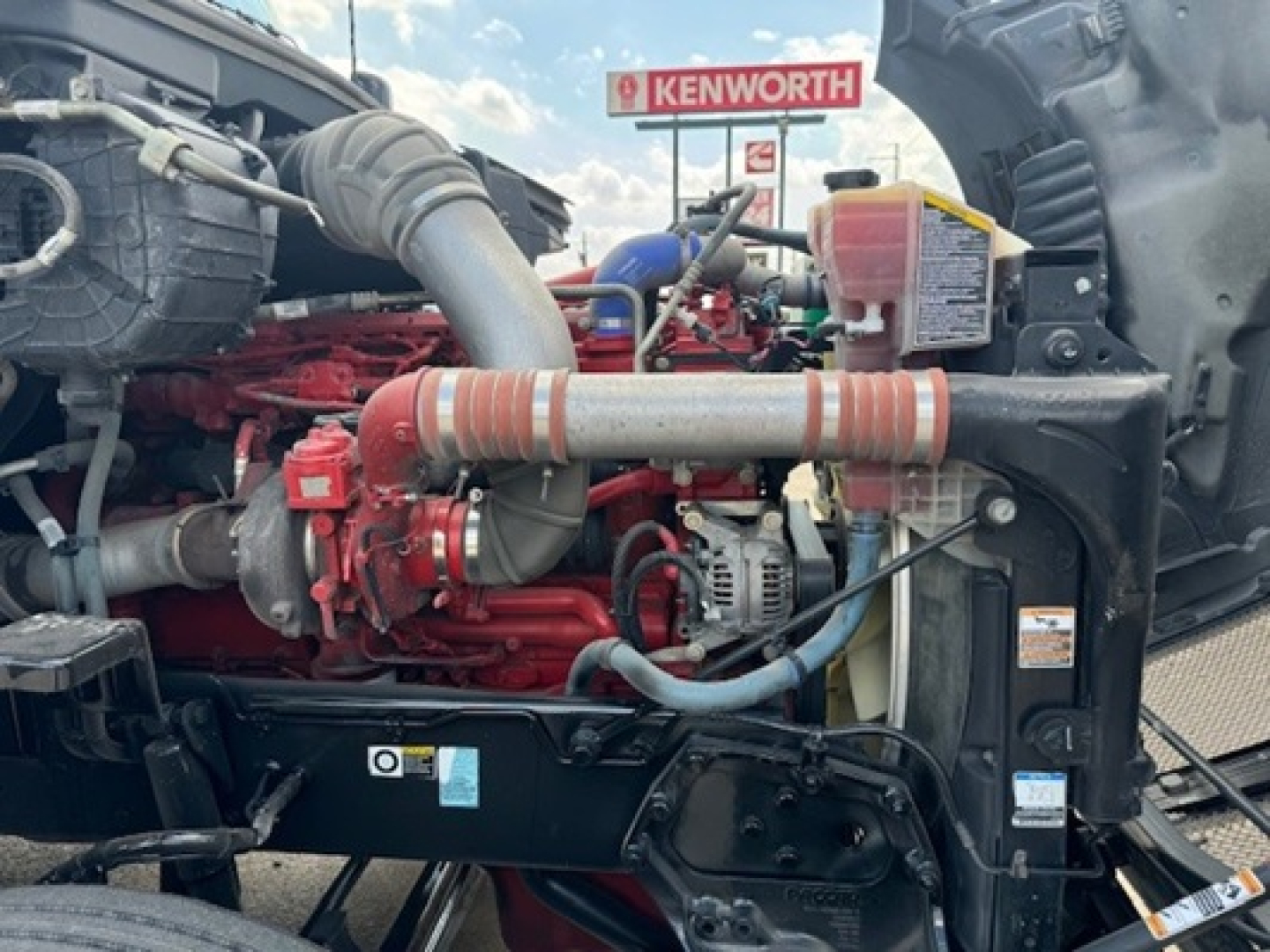 Kenworth T680 engine bay view with red engine block, hoses, and intake piping visible.