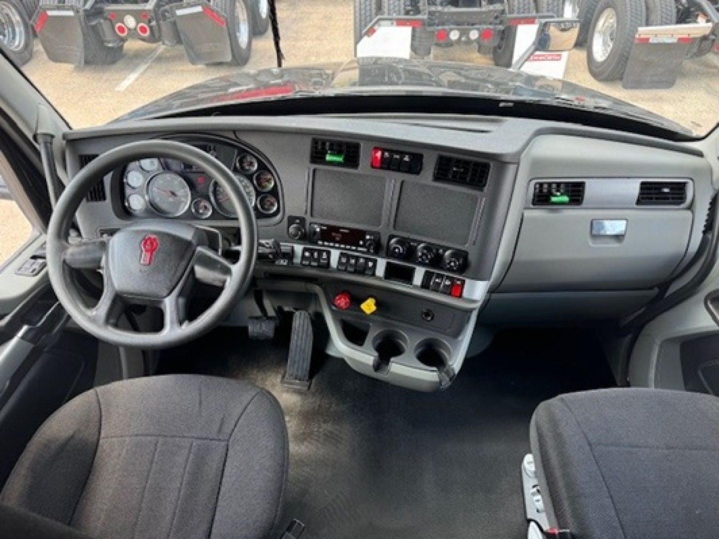 Cab interior of a 2022 Kenworth T680 with driver and passenger seats, steering wheel, dashboard, and center console visible.