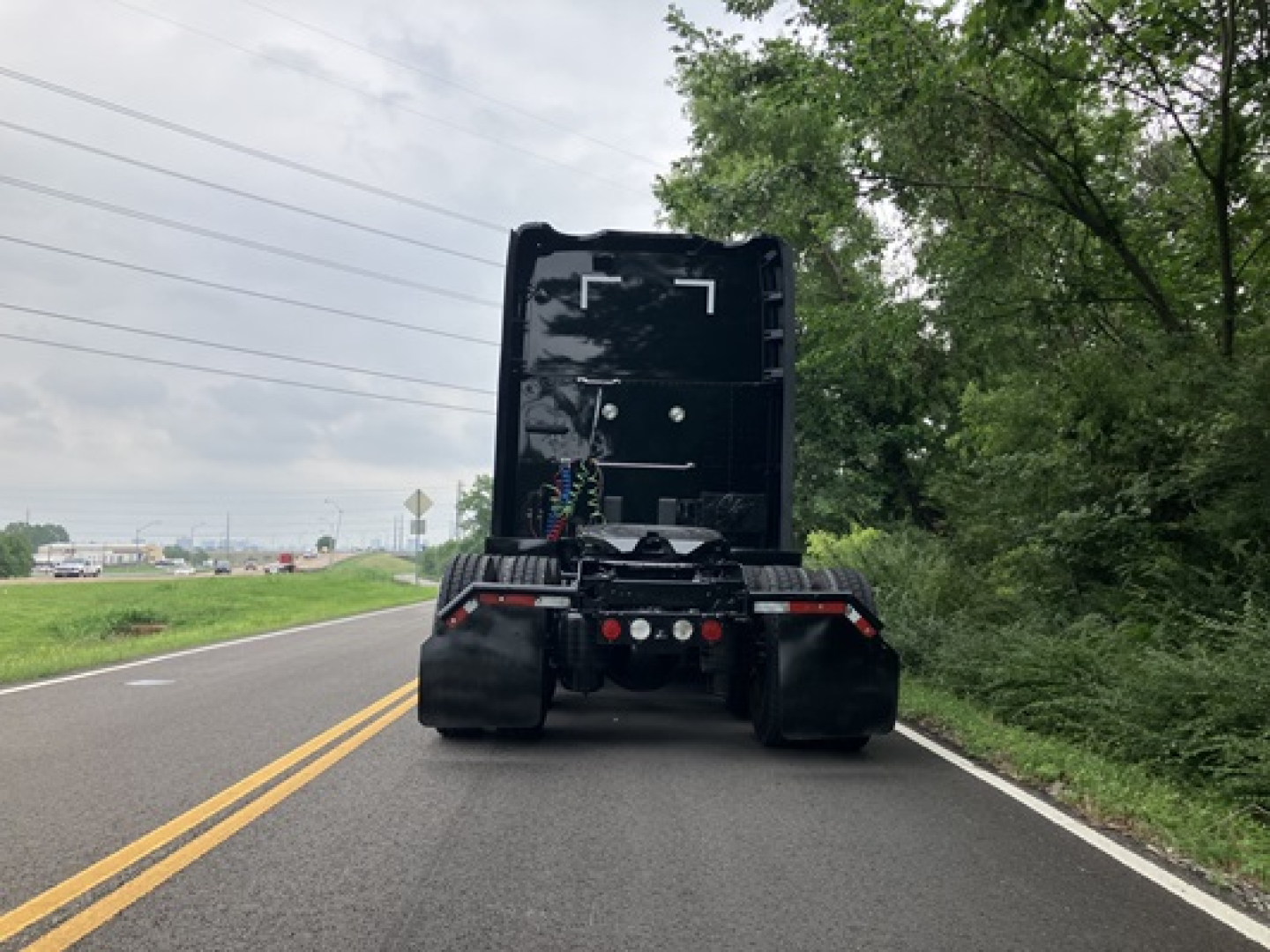 Rear view of a 2022 Kenworth T680 truck with fifth wheel and exposed wiring in a sleeper cab area, back of tractor on a two-lane road.