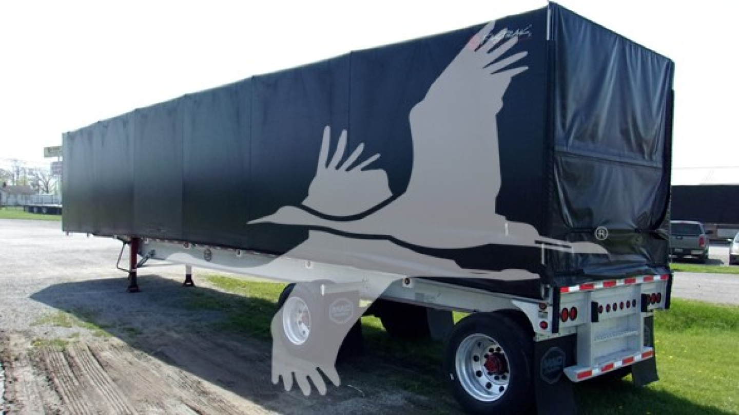 Curtainside trailer showing blue fabric cover with white graphic of hands and birds and trailer wheels in view.