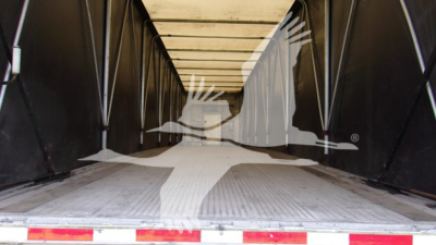 Trailer interior showing cargo floor with side walls and ceiling beams, viewed from rear with open doors.