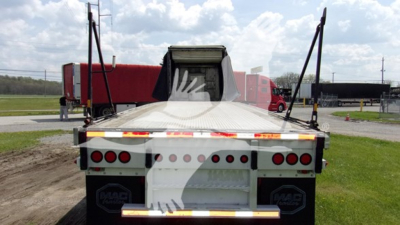 Rear view of a curtain-side trailer with MAC branding on mud flaps and rear bumper, showing multiple red tail lights and reflective strips.