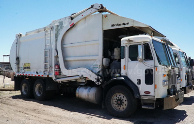 Truck body side view showing large garbage compactor with 'MEMPHIS' branding and rear loader, white cab with side mirrors, dual rear axles.