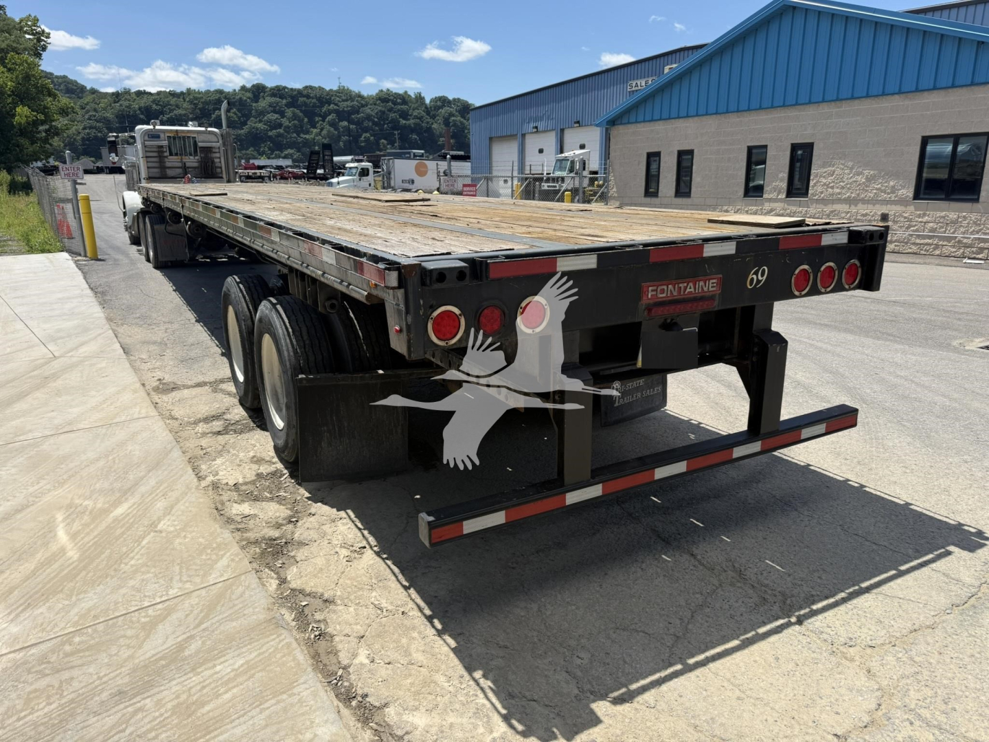 Fontaine flatbed trailer showing rear with taillights and 69 plate, wooden deck, dual rear axles, and jump-looking bumper.