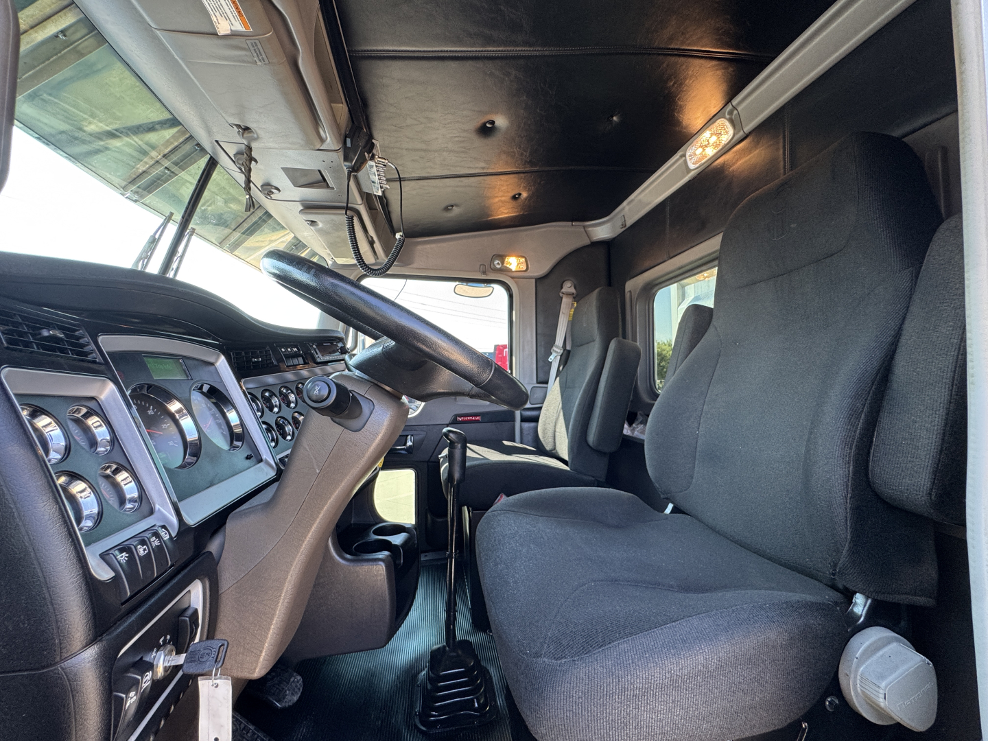 Kenworth W900L truck cabin interior showing steering wheel, dashboard gauges, and driver seat.
