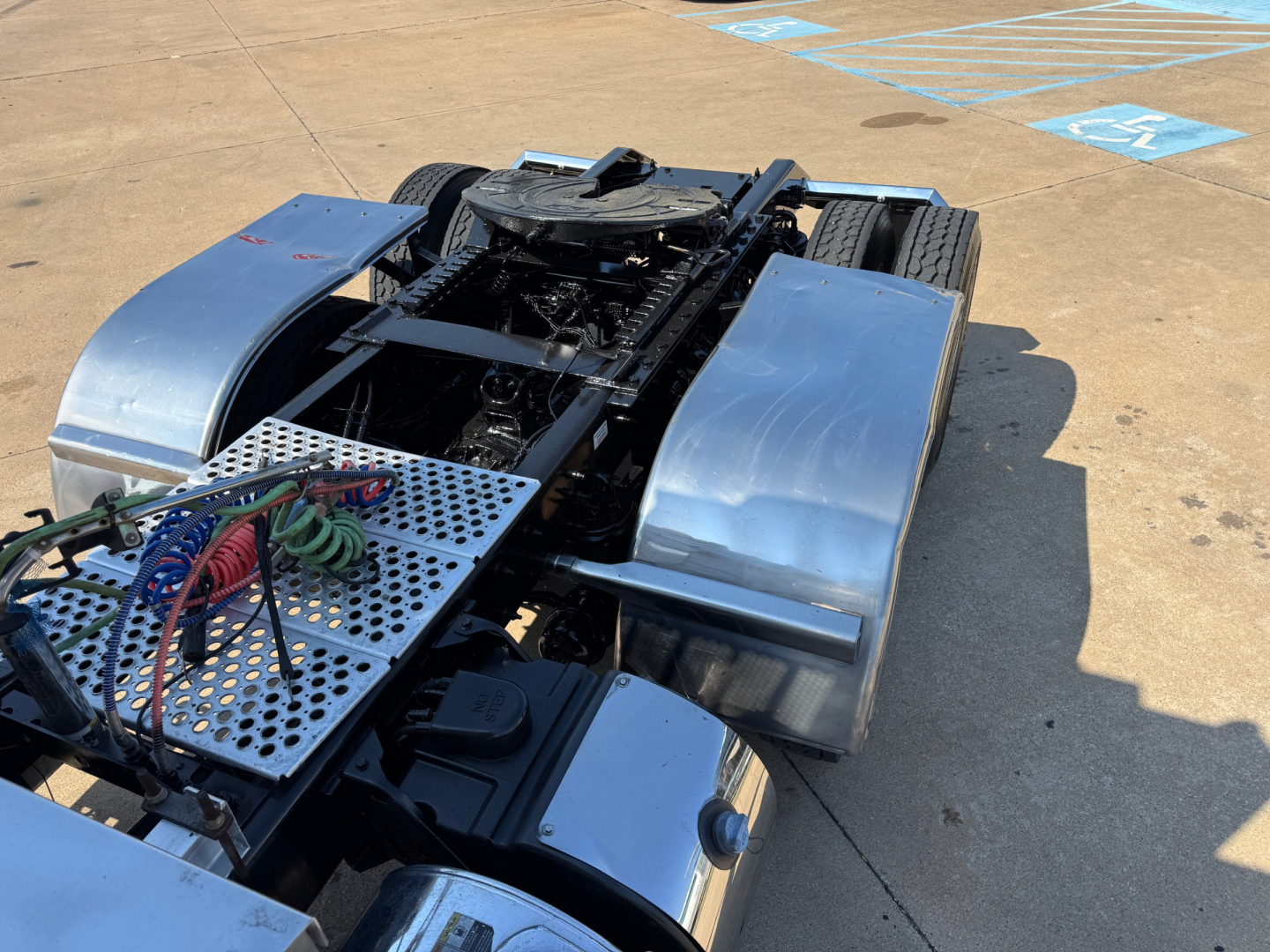 Kenworth W900L chassis with exposed fifth wheel area and metal steps, dual rear wheels, chrome fuel tanks, and blue fenders visible