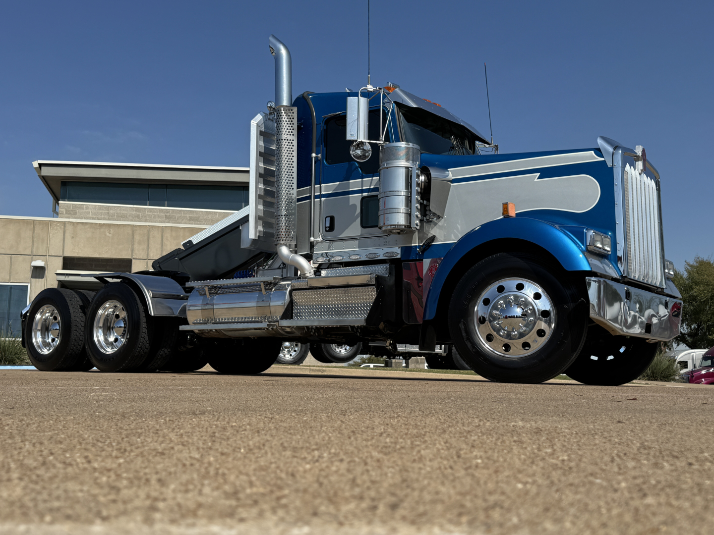 Kenworth W900L conventional daycab truck in blue with chrome accents, chrome exhaust stacks, dual rear axles, and polished wheels.