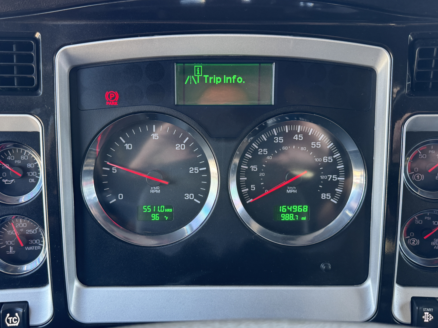 Kenworth W900L dash cluster showing two large gauges with green trip info on screen and multiple indicators.
