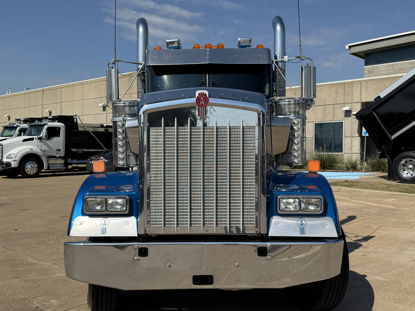 Kenworth W900L conventional daycab front view showing large chrome grille, dual tall exhaust stacks, rectangular headlights, blue fenders, and chrome bumper.