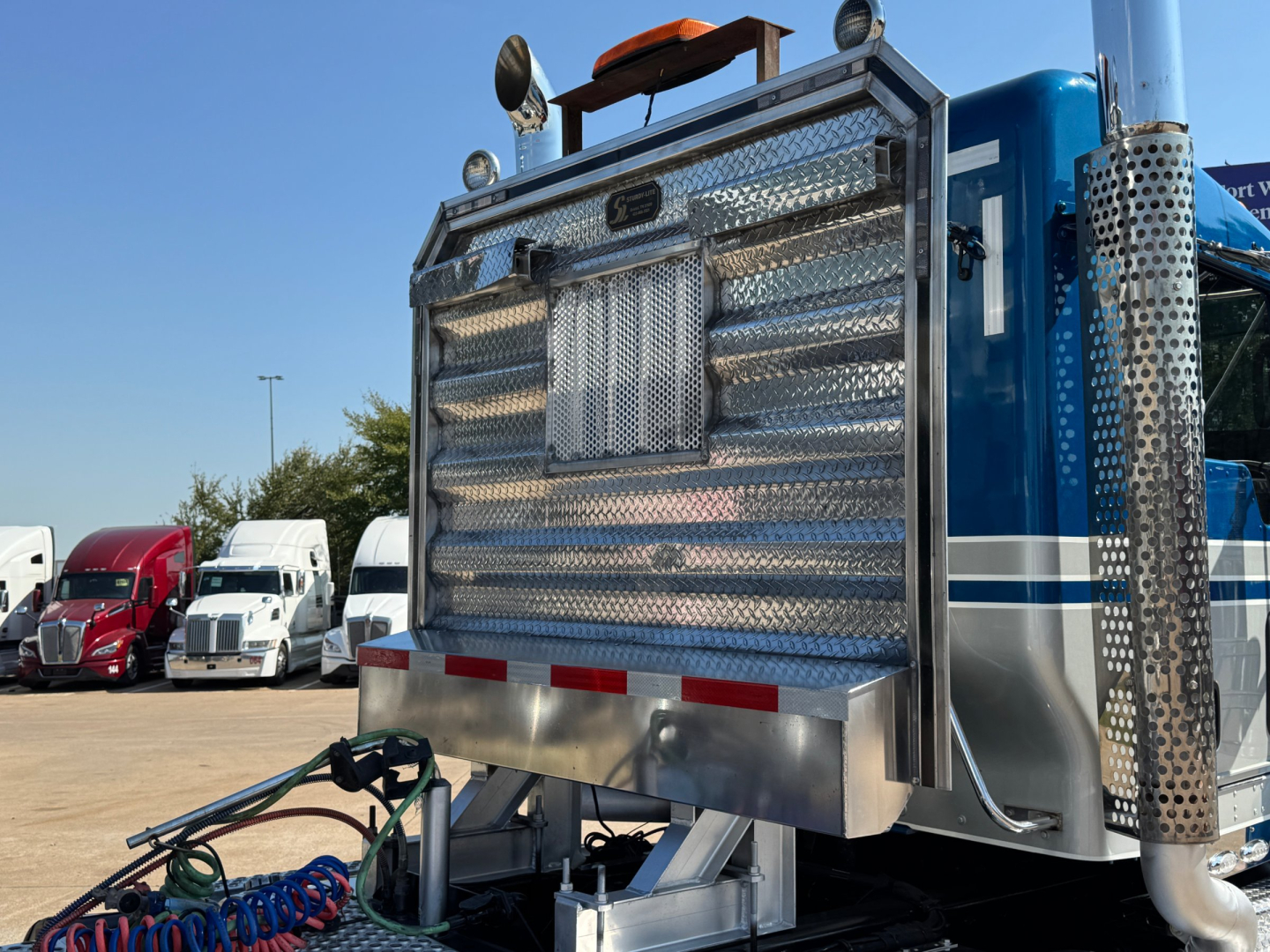 Kenworth W900L truck cab rear cargo area with diamond-plate metal and chrome exhaust stacks visible