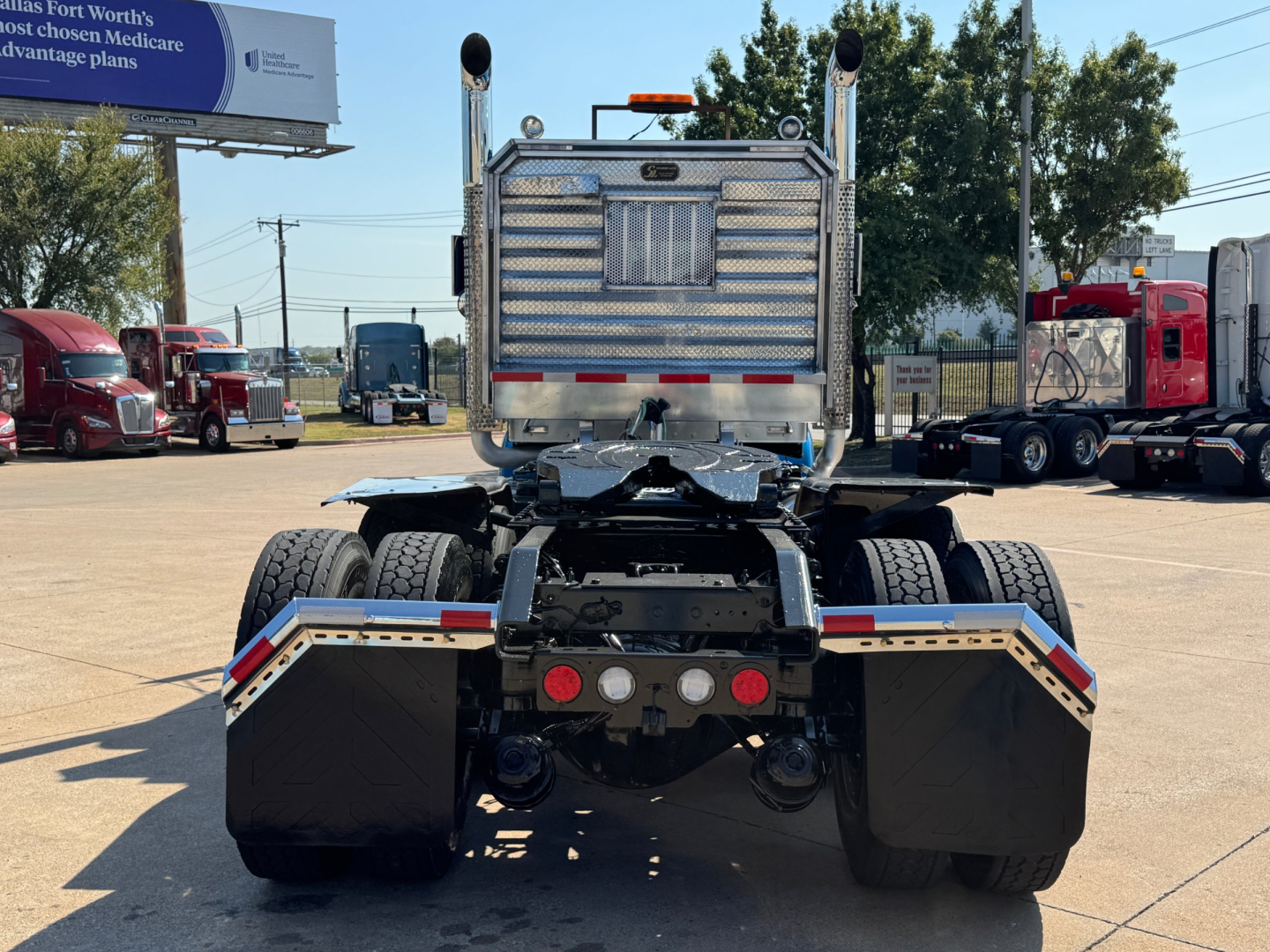 Kenworth W900L chassis rear view showing dual rear axles and mud flaps, aluminum fuel tanks, rear bumper, and fifth wheel under cab.