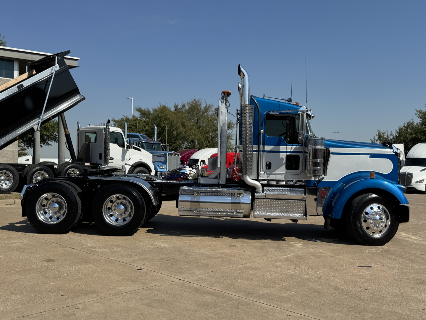 Kenworth W900L conventional daycab truck side view showing chrome exhaust stacks and sleeper cab with blue fenders and dual rear axles.