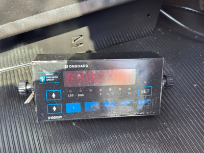 Kenworth W900L interior area with a digital on-board scale module showing numeric display and blue buttons labeled 1-9, AUTO, SET, and 9100GW.