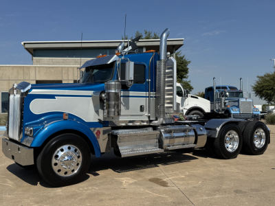 Kenworth W900L truck side view showing chrome fuel tanks, dual rear axles, blue and silver paint with chrome exhaust stacks.