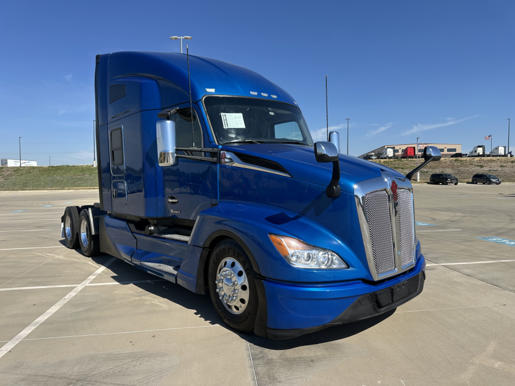 Blue 2022 Kenworth T680 tractor-trailer front-left view with sleeper cab, chrome mirrors, and dual rear axles; no visible text readable on signage in cab window.