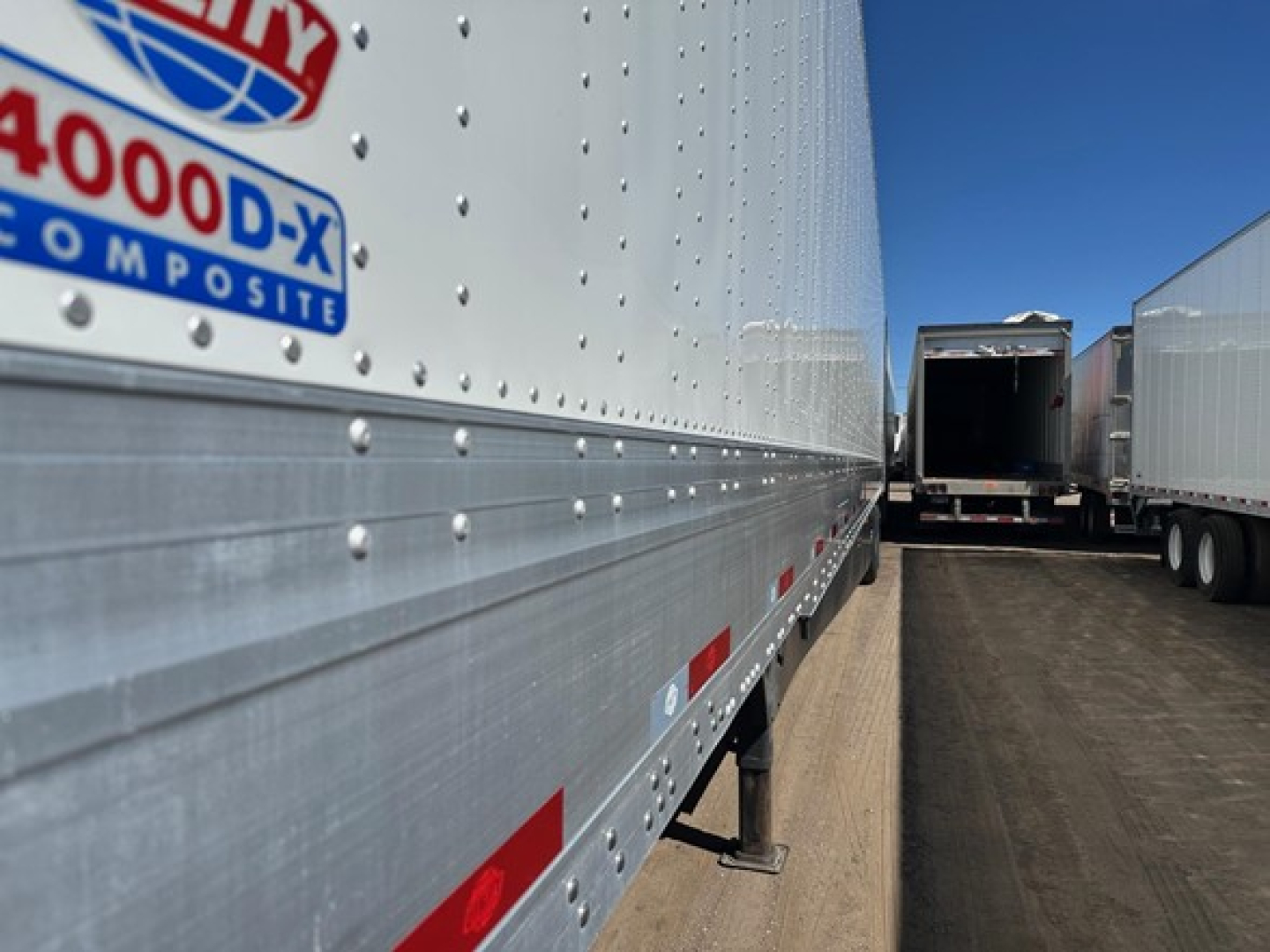 Trailer side with 4000-D-X composite sticker and riveted aluminum siding, showing a ramp-style trailer in a yard.