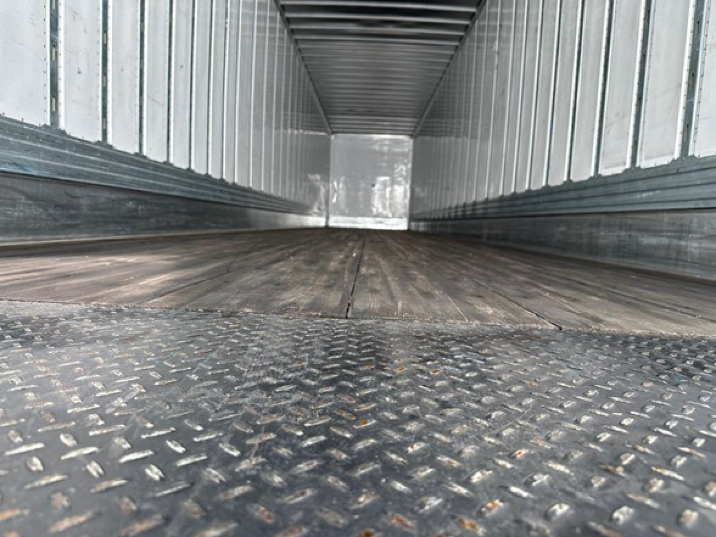 Interior of a Utility 4000dx trailer showing metal diamond plate floor and side walls, empty cargo space, taken from near floor level.