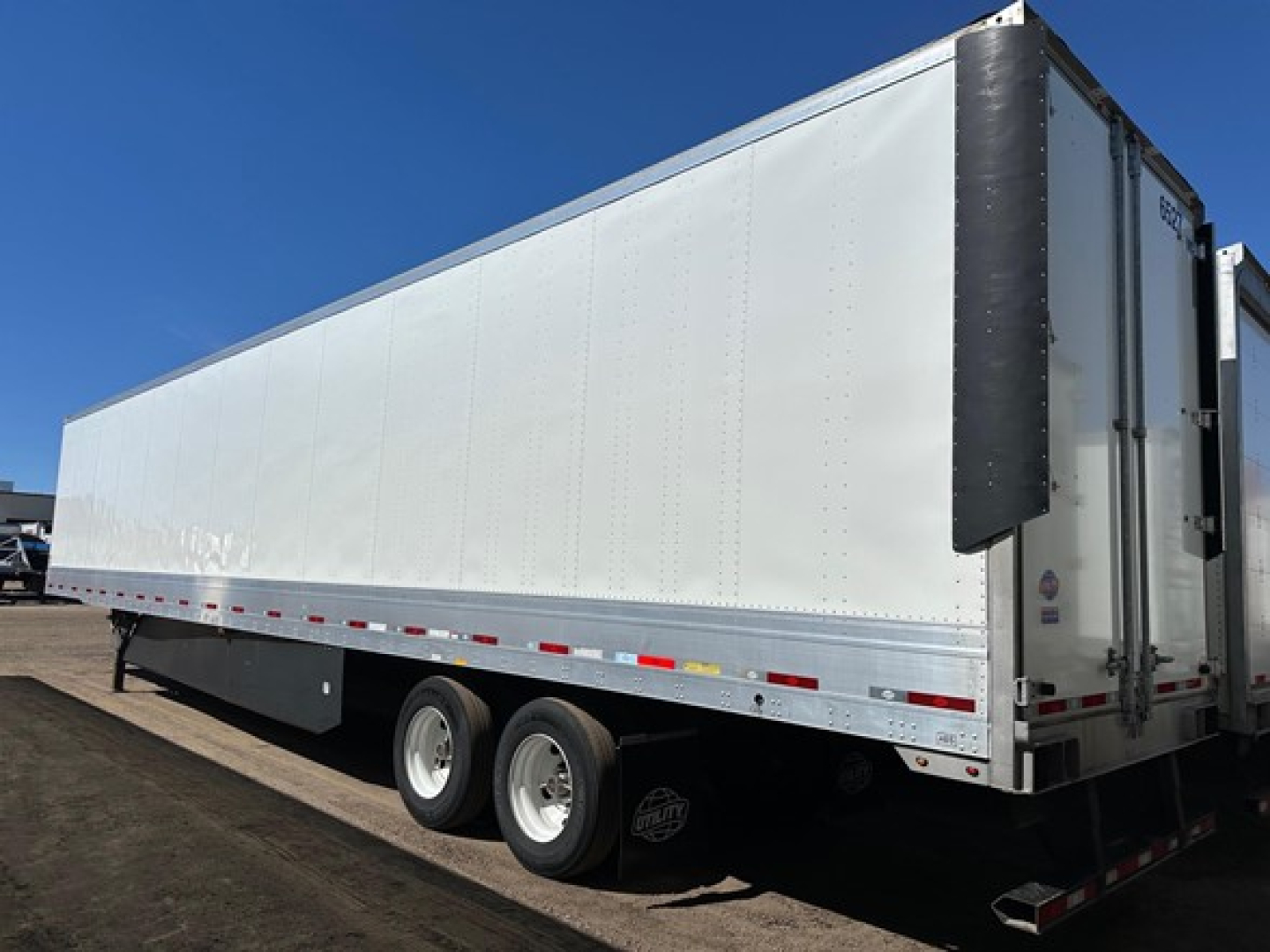Trailer side view showing Utility 4000DX/TBR model? long white enclosed trailer with dual rear doors, flat side panels, and supporting wheels.