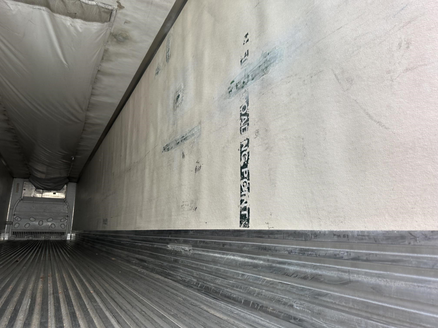 Trailer interior showing ribbed aluminum floor, side walls with white insulation, and a small front cab area visible at far end.