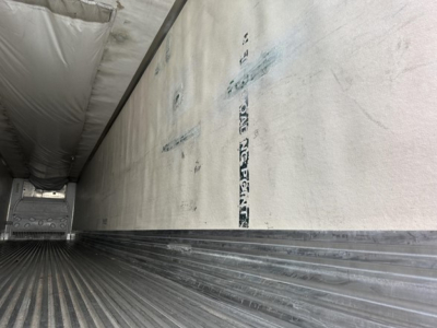 Trailer interior with ribbed metal floor and sidewall insulation, showing a reefer unit interior and rear stair area edge; faint vertical lettering on side wall.