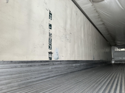Trailer interior with ribbed aluminum floor and white insulated wall showing vertical faded text. Image indicates the cargo area of a refrigerated trailer.