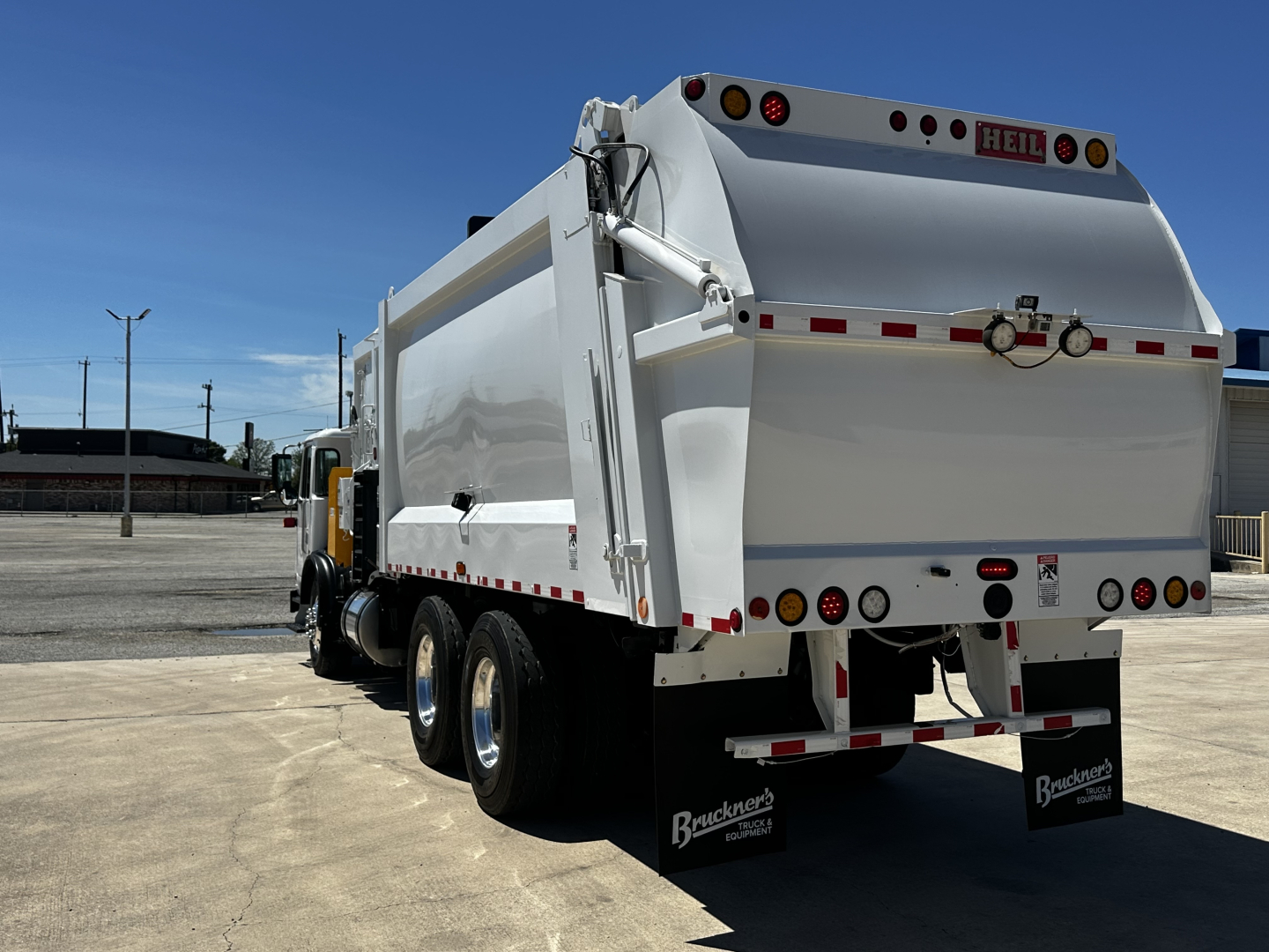 Rear view of a white Autocar XPEDITOR dump truck with dual rear axles, HEIL logo, reflective tape, and Brackett’s mud flaps.